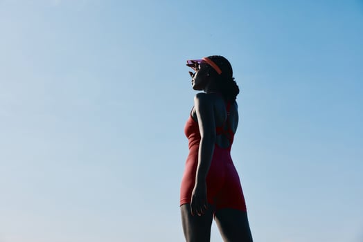 A stylish woman in a red swimsuit stands confidently against a bright blue sky, promoting a sense of photo