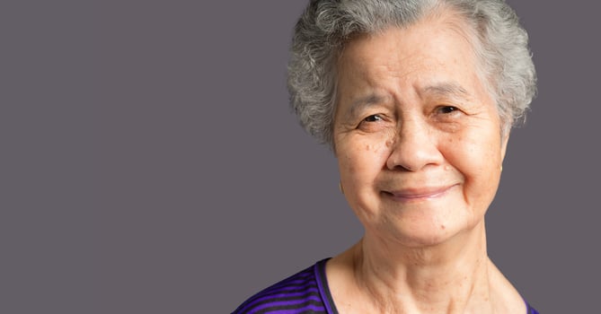 Cheerful an elderly Asian woman with short gray hair looking at the camera with a smile while standing on gray background in the studio. photo