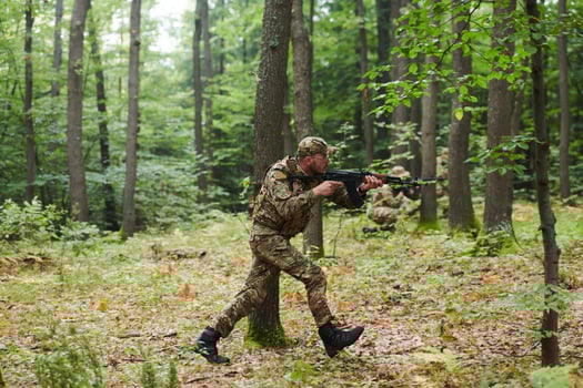 An elite soldier, camouflaged and stealthily navigating through dangerous woodland terrain, executes a covert mission in a secluded forest area photo