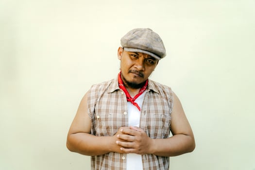 Half body portrait of adult Southeast Asian man in sleeveless shirt, bandana and newsboy hat. Macho male model with beard and mustache looking serious and fierce isolated on beige background. photo