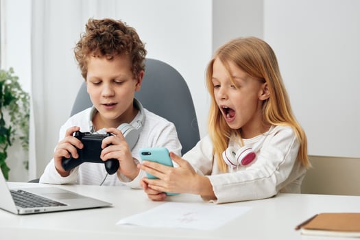 Happy Caucasian children studying together at home with their laptops and headphones, immersed in photo