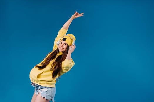 A pregnant girl in a yellow jacket and headphones stands on a blue background photo
