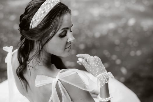An elegant bride in a white dress, gloves and bare feet is sitting near a waterfall in the Park enjoying nature.A model in a wedding dress and gloves at a nature Park.Belarus. black and white photo