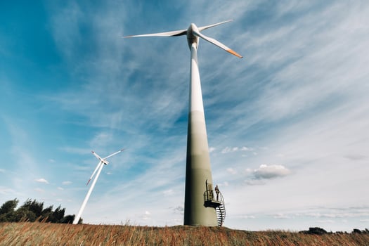 A man in a business suit with a green Golf shirt stands next to a windmill against the background of the field and the blue sky.Businessman near the windmills.Modern concept of the future. photo