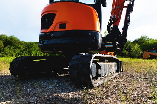 rear view of small excavator with rubber tracks in a clearing surrounded by greenery in summer photo