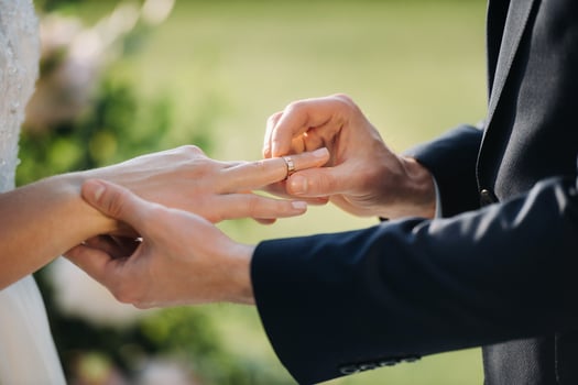The groom puts an engagement ring on the bride's finger on their wedding day photo