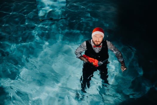 A man in a Santa Claus suit and hat with a red gun in his hands. Santa Claus is swimming underwater with a gun.Christmas concept photo