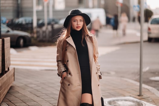 Stylish young woman in a beige coat in a black hat on a city street. Women's street fashion. Autumn clothing.Urban style photo