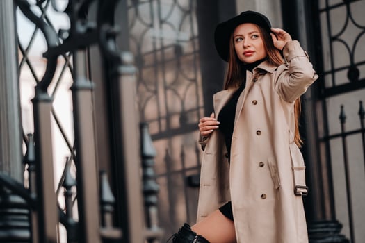 Stylish young woman in a beige coat in a black hat on a city street. Women's street fashion. Autumn clothing.Urban style photo
