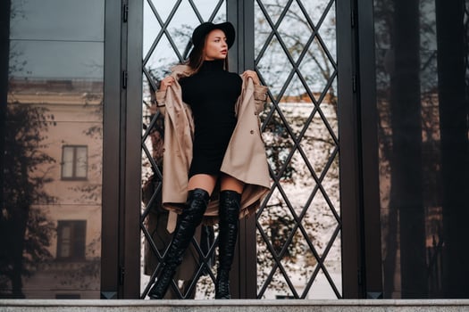 Stylish young woman in a beige coat in a black hat on a city street. Women's street fashion. Autumn clothing.Urban style photo