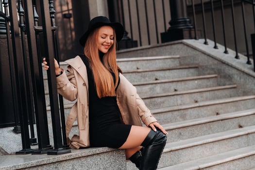 Stylish young woman in a beige coat in a black hat on a city street. Women's street fashion. Autumn clothing.Urban style photo