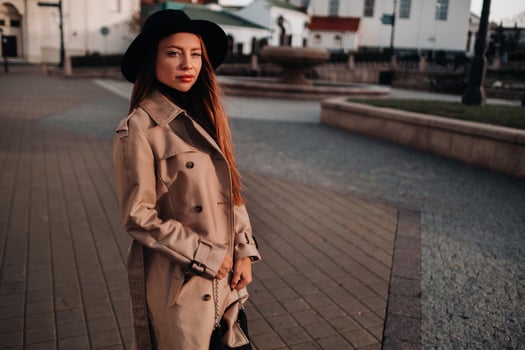 Stylish young woman in a beige coat in a black hat on a city street. Women's street fashion. Autumn clothing.Urban style photo