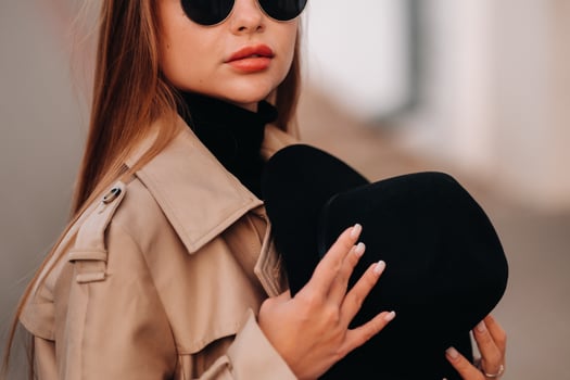 Stylish young woman in a beige coat and a black hat in his hands and glasses on a city street. Women's street fashion. Autumn clothing.Urban style. photo