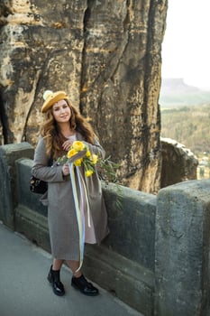 a girl in a gray coat and hat with a bouquet of flowers on the background of mountains and gorges in Swiss Saxony, Germany, Bastei photo