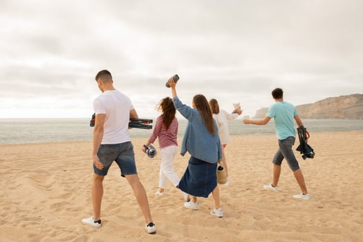 A group of friends walks along the sandy beach, holding cameras and other items, enjoying a fun outing during sunset. The ocean waves gently lap against the shore in the background. photo