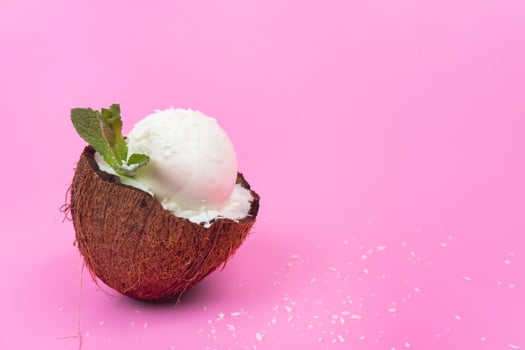 Vanilla ice cream balls in fresh coconut halves, decorated with mint leaves on a pink background photo