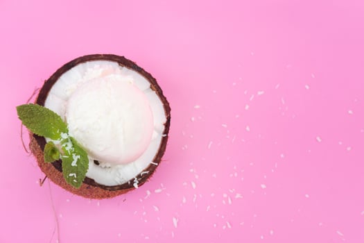 Vanilla ice cream balls in fresh coconut halves, decorated with mint leaves on a pink background photo
