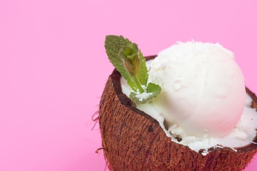 Vanilla ice cream balls in fresh coconut halves, decorated with mint leaves on a pink background photo