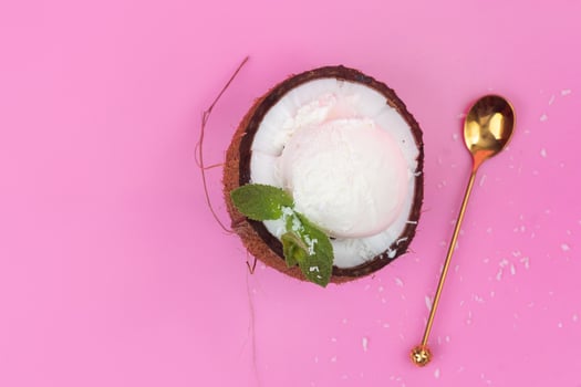 Vanilla ice cream balls in a fresh coconut half decorated with mint leaves with a spoon on a pink background photo