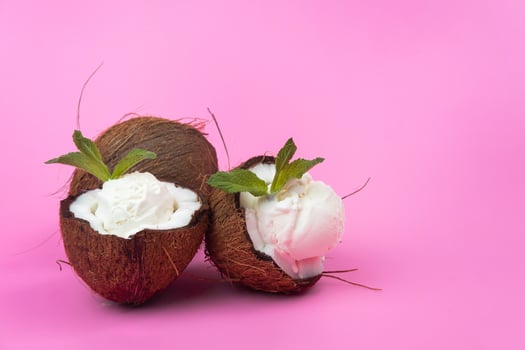 Vanilla ice cream balls in fresh coconut halves decorated with mint leaves on a pink background photo