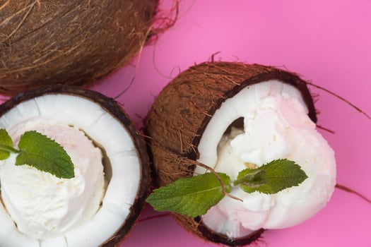 Vanilla ice cream balls in fresh coconut halves decorated with mint leaves on a pink background photo