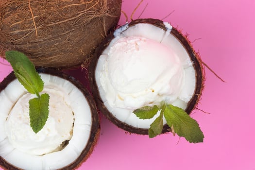 Vanilla ice cream balls in fresh coconut halves decorated with mint leaves on a pink background photo