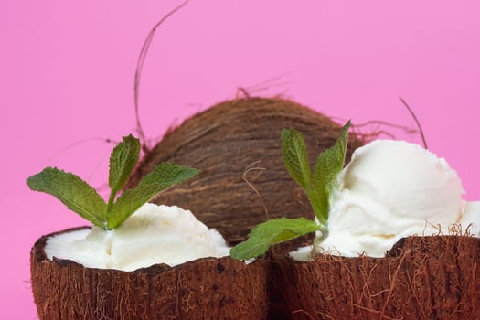 Vanilla ice cream balls in fresh coconut halves decorated with mint leaves on a pink background photo