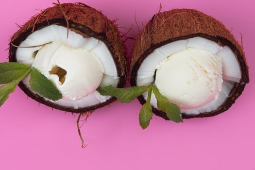 Vanilla ice cream balls in fresh coconut halves decorated with mint leaves on a pink background photo