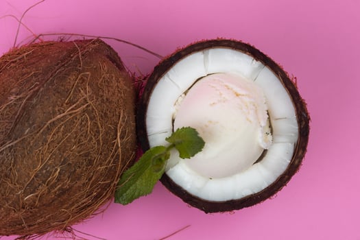 Vanilla ice cream balls in fresh coconut halves decorated with mint leaves on a pink background photo