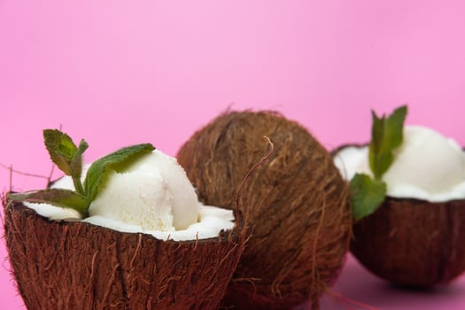 Vanilla ice cream balls in fresh coconut halves decorated with mint leaves on a pink background photo