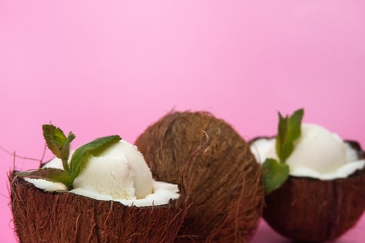 Vanilla ice cream balls in fresh coconut halves decorated with mint leaves on a pink background photo