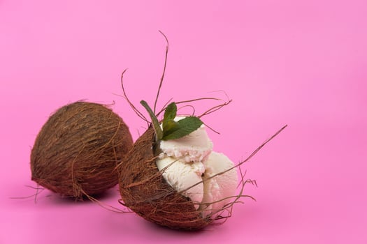 Vanilla ice cream balls in an empty coconut decorated with mint leaves on a pink background photo