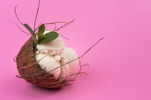 Vanilla ice cream balls in an empty coconut decorated with mint leaves on a pink background photo