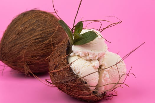 Vanilla ice cream balls in an empty coconut decorated with mint leaves on a pink background photo