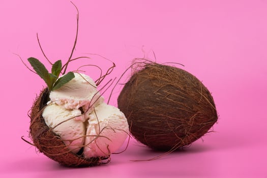 Vanilla ice cream balls in an empty coconut decorated with mint leaves on a pink background photo