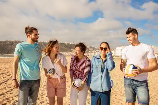 A group of five friends enjoys a lively day at the beach, engaging in playful activities and sharing laughter against a backdrop of clouds and coastline scenery. photo