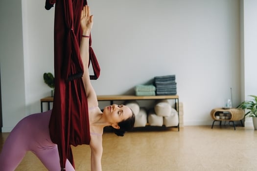 A woman in pink clothes does yoga on a suspended burgundy hammock in a bright gym photo