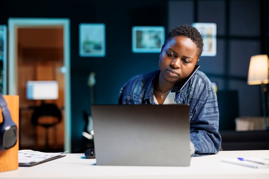 Dedicated female freelancer working from home, having business phone calls while using digital laptop. African american college student utilizes modern technology for online communication. photo