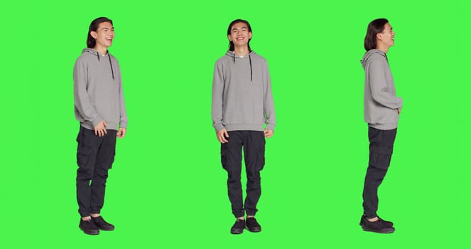 Cheerful male model laughing in studio, posing and being positive against full body greenscreen backdrop. Asian man smiling in studio, showing amusing funny expressions, relaxed guy. photo