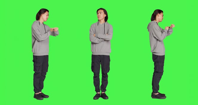 Impatient adult waiting for something in studio, looking around and checking hour on wristwatch over greenscreen backdrop. Asian person being unhappy and irritated, looks at watch. photo