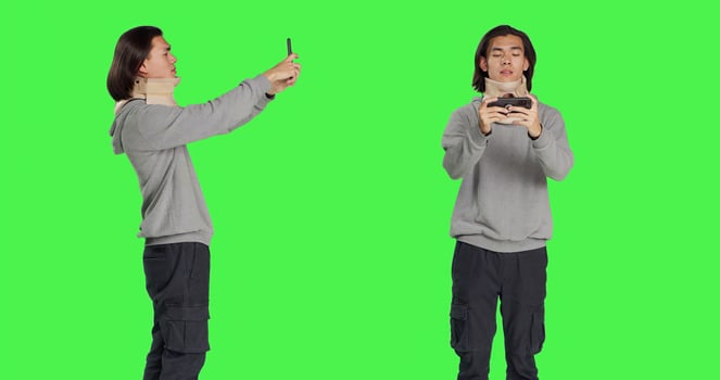 Wounded guy wearing cervical collar on videocall across greenscreen, engaging on remote internet discussion while wearing medical neck support after injury. Man suffered vertebral lesion. photo