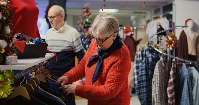 Elderly woman browsing through clothes in festive Christmas decorated shopping mall fashion shop men section, looking for blazer to gift husband for upcoming xmas holiday season photo