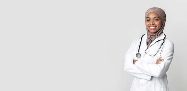 Medical Career For Muslim Women. Portrait Of Black Islamic Women Doctor Standing With Folded Arms And Looking At Camera, Light Background photo