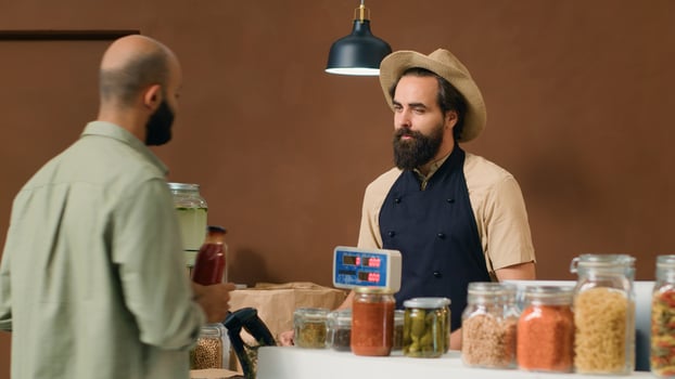 Vendor at checkout scanning and weighting products to sell to frequent client in local zero waste store. Young man placing vegetables on scale, selling locally grown produce to buyer. photo