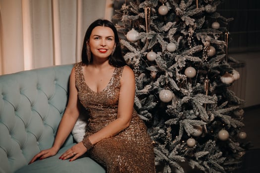 A girl in an evening dress is sitting on the sofa near the Christmas tree photo