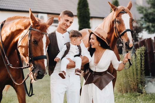 A family in white clothes with their son stand near two beautiful horses in nature. A stylish couple with a child are photographed with horses photo