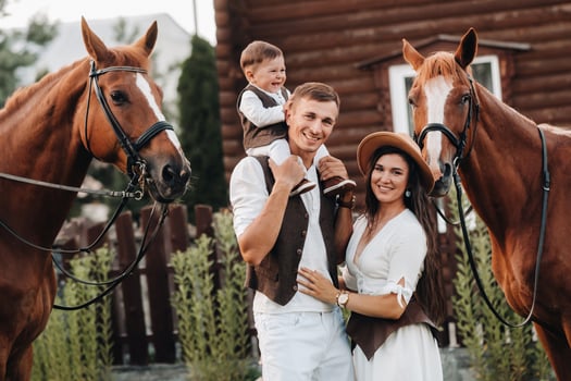 A family in white clothes with their son stand near two beautiful horses in nature. A stylish couple with a child are photographed with horses photo