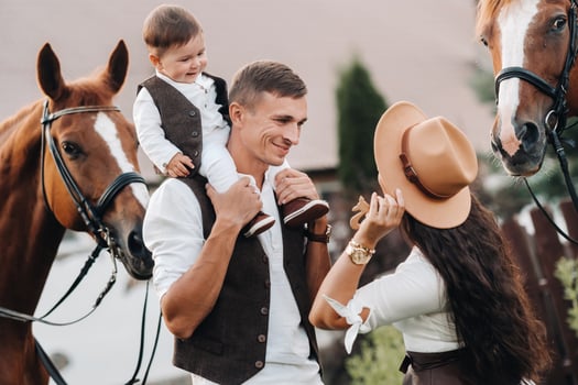A family in white clothes with their son stand near two beautiful horses in nature. A stylish couple with a child are photographed with horses photo