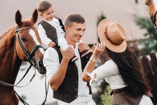A family in white clothes with their son stand near two beautiful horses in nature. A stylish couple with a child are photographed with horses photo