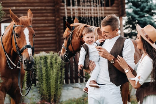 A family in white clothes with their son stand near two beautiful horses in nature. A stylish couple with a child are photographed with horses photo